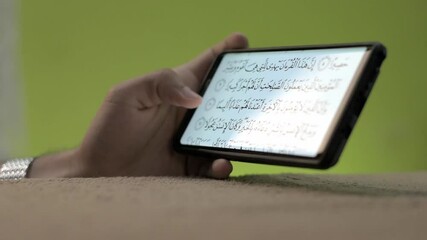 Wall Mural - A hand scrolling a Quran recitation using a smartphone application on a green background