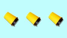 Three Bright Yellow Paper Coffee Cups With Aromatic Robusta Coffee Rotate On A Light Blue Background. Seamless Video