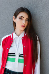 Wall Mural - brunette woman in black and red jacket looking at camera near grey wall