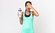 young hispanic woman looking shocked, scared or terrified, covering face with hand and holding a water bottle. fitness concept