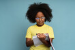 Portrait of positive genius child, clever little girl wearing glasses and looking at her notebook with smart happy expression. Indoor studio shot isolated on blue background