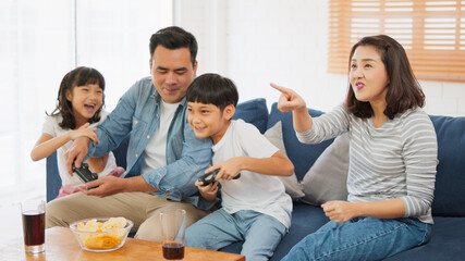 Young happy Asian family use joy controller, play video game together at home. Weekend holiday leisure party, people having fun, or home domestic activity lifestyle concept