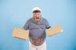 Excited mature man with overweight in sailor costume holds blank cardboard boxes of pizza standing on light blue background in studio