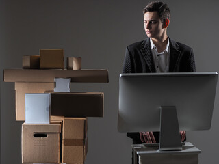 Poster - Parcel delivery business. A man at a laptop next to cardboard boxes. The young man prepares parcels for shipment. A young businessman is engaged in the delivery of goods.