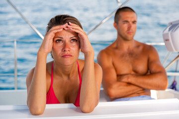 Wall Mural - Frustrated woman sitting separately at sailboat during sea cruise, having problems in relationship with husband..