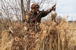 a hunter with a shot duck in his hands gets up from a camouflaged hideout