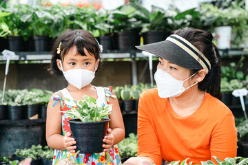 Wall Mural - Small girl with her mother wearing protective face mask at tree store.