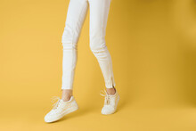 Female Legs In White Pants Sneakers Fashion Yellow Background