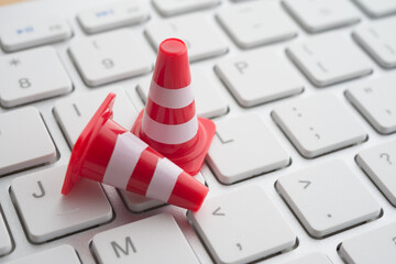 Maintenance, repair, under construction in computer system from virus or ransomware concept. Close up orange white traffic warning cones or pylon on keyboard computer background with copy space.