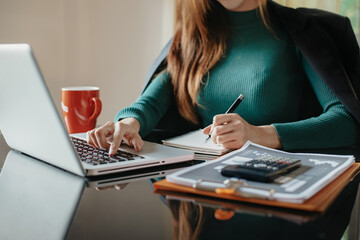 Businesswomen using laptop and writing note on desk in modern office.