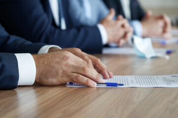 A man in an elegant suit holds his hands on the table, next to a document, during a work meeting. Without a face. Boss, deputy, politician, official, lawyer or businessman