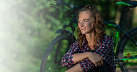 Portrait of a cheerful young woman in a shirt looking to the side against the background of a bicycle on a sunny summer day with a white place with copy space. Banner