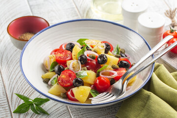 Poster - Close-up of Mediterranean salad.  Made with boiled potatoes, tomatoes, onions, oregano, capers, black olives, basil leaves. White wooden background.