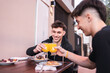 Two friends toasting with orange juice sitting at an outdoor table in a bar.