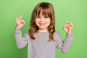 Wall Mural - Photo of joyful small blond hair girl show okey wear striped shirt isolated on green color backgound