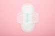 New opened white sanitary towel on light pink table background. Pastel color. Closeup. Female hygiene. Top down view.