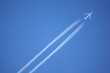 Large four engine passenger supersonic airplane flying from left to right high in blue cloudless sky leaving long white tracks