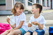 Schoolchildren boy and girl laugh and eat their lunch, snack, breakfast in the school yard. Food for children in educational institutions, kindergartens.