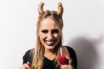 Wall Mural - Close-up shot of cheerful girl drinking blood in halloween. Carefree vampire with blonde hair posing at carnival.