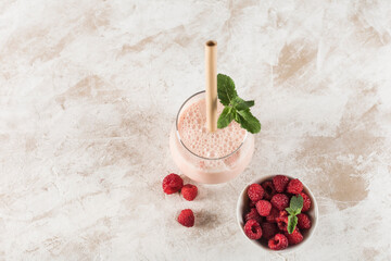 Wall Mural - A glass with a Lassi drink with raspberries, mint and a bamboo tube on a light background.