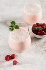 Wall Mural - Two glasses with a Lassi drink with raspberries, mint and a bamboo tube on a light background.