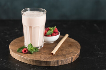 Wall Mural - Lassi drink with raspberries in a glass with mint and a bamboo tube on a wooden board.