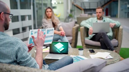 Wall Mural - Startup business team of three sitting in office lobby and planning work. Marketing manager explaining ideas and showing printed web and mobile app interface templates to colleagues, focus on paper