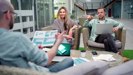 Wall Mural - Startup business team of three sitting in office lobby and planning work. Marketing manager explaining ideas and showing printed web interface templates to colleagues