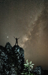 Wall Mural - silhouette of person is standing on the top of the hill next to the milky way galaxy with his hands 
