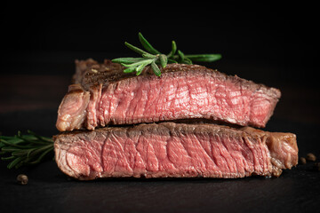 Side view of juicy roasted steak sliced in two parts made of grain-fed beef meat decorated with fresh rosemary sprig and pepper cooked to a medium level with fried crust with stripes. Horizontal