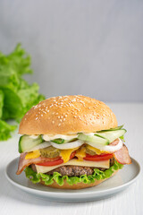 Wall Mural - Hamburger, also burger, made of cooked grilled patties of ground beef meat, lettuce,  tomato, onion, pickles, bacon, cheese and cucumber inside fresh sliced bun served on plate on white wooden table