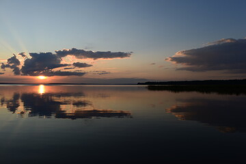Wall Mural - Bright sun rays from the clouds at sunset are reflected in the tranquil water of the lake