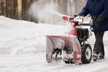 A Man With A Red Snowplow Cleans The Lawn In Front Of The House From Snow. Clearing The Area From Snowfall.