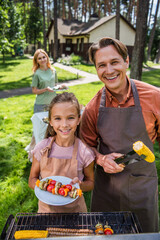 Wall Mural - Father and smiling kid in aprons holding grilled vegetables during picnic