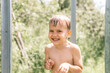 little contented wet four year old kid boy with water drops on his skin after rinsing with cold water in a outdoor shower in nature in a garden in the village