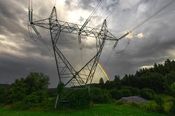 Electrical power voltage pylon or tower standing in the green with magnificent rainbow in behind.