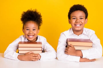Wall Mural - Photo of cheerful young dark skin friends children sit table hold books smile isolated on yellow color background