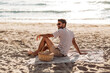 © Syda Productions - summer holidays and people concept - portrait of happy smiling young man in sunglasses sitting on blanket with picnic basket on beach
