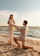 © Syda Productions - love and people concept - smiling young man with engagement ring making proposal to happy woman on beach