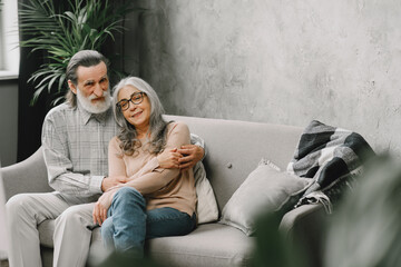 Wall Mural - Senior couple in casual clothes sitting on couch in living room