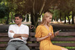 Young woman with smartphone ignoring her boyfriend in park. Boring date