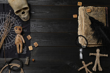 Wall Mural - Voodoo doll with pins surrounded by ceremonial items on black wooden table, flat lay. Space for text