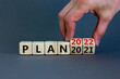 © Dzmitry - 2022 plan new year symbol. Businessman turns a wooden cube and changes words 'Plan 2021' to 'Plan 2022'. Beautiful grey background, copy space. Business, 2022 plan new year concept.