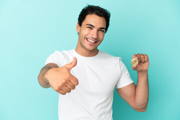 Sticker - Young man holding a Bitcoin over isolated blue background with thumbs up because something good has happened