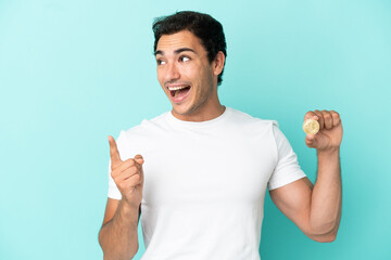 Sticker - Young man holding a Bitcoin over isolated blue background intending to realizes the solution while lifting a finger up