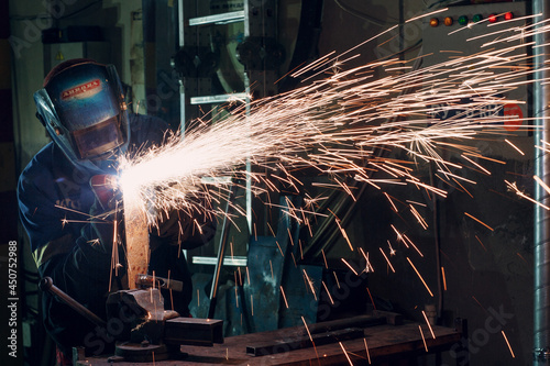 Man in mask cuts metal with plasma cutter. Helmet and spakrs.