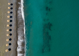  Aerial view from a flying drone of beach umbrellas in a row on an empty beach with braking waves.