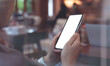 © tippapatt - Cell phone mockup image blank white screen.  Woman hand holding, using mobile phone in coffee shop, close up