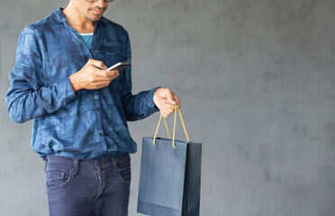 Lifestyle man using mobile phone and holding shopping bag with copy space gray wall background, Application online shopping design banner concept