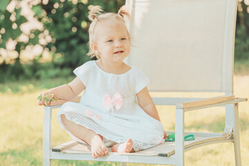 Sticker - caucasian infant girl blonde sitting on a chair in the garden in summer